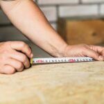 Personne mesurant un panneau de fibre de bois sous des rampants de toiture avec une calculette.