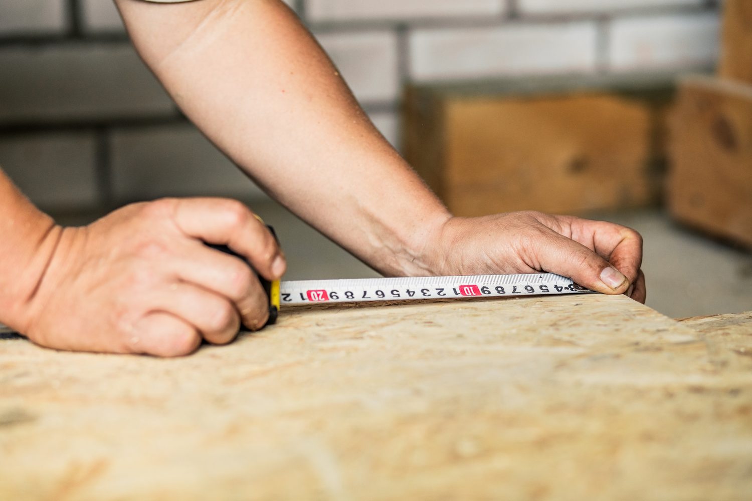 Personne mesurant un panneau de fibre de bois sous des rampants de toiture avec une calculette.